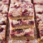 Hands pressing cranberry bliss bar dough evenly into a square baking dish lined with parchment paper